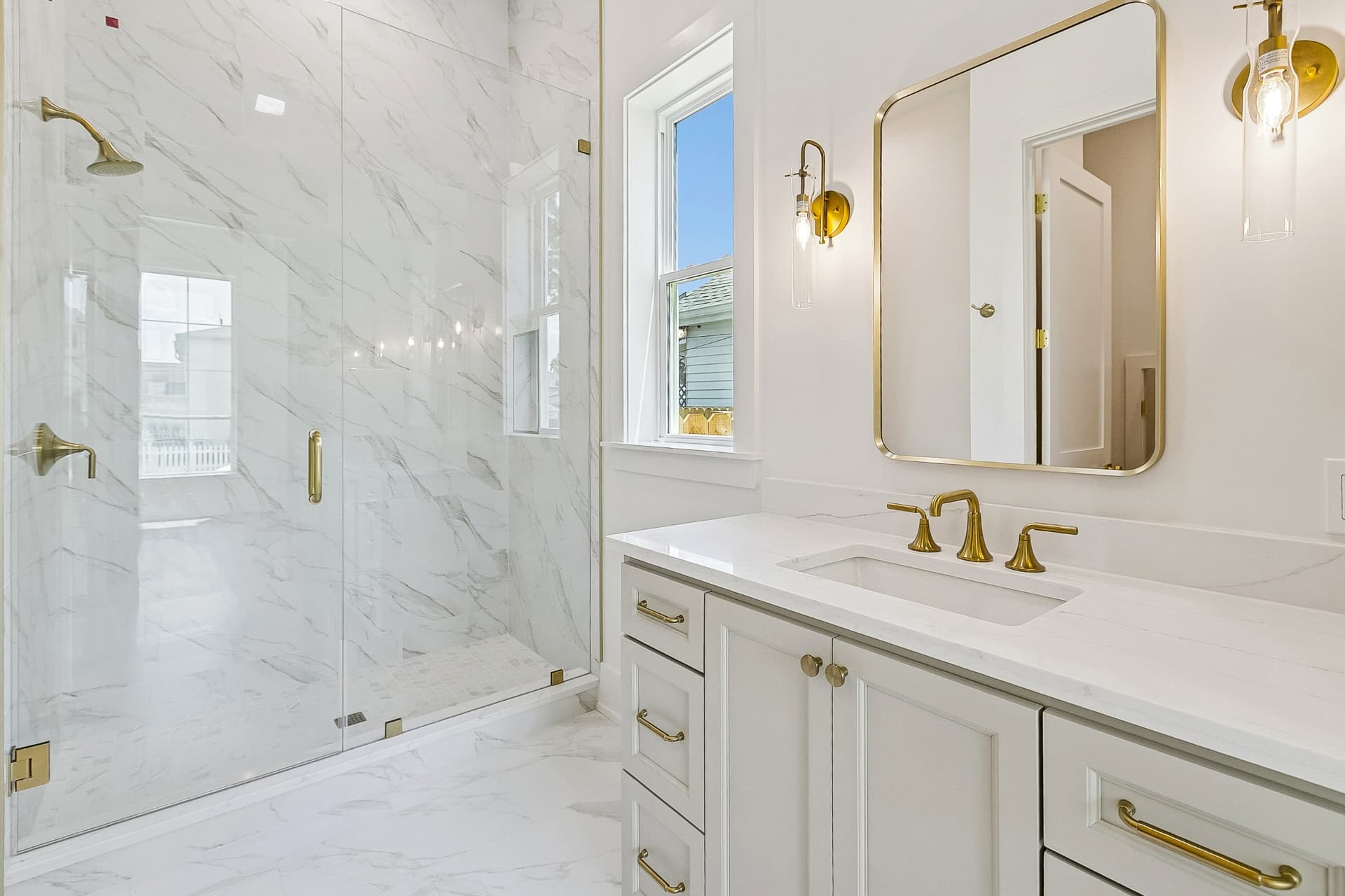 Marble bath with glass shower and brass lighting